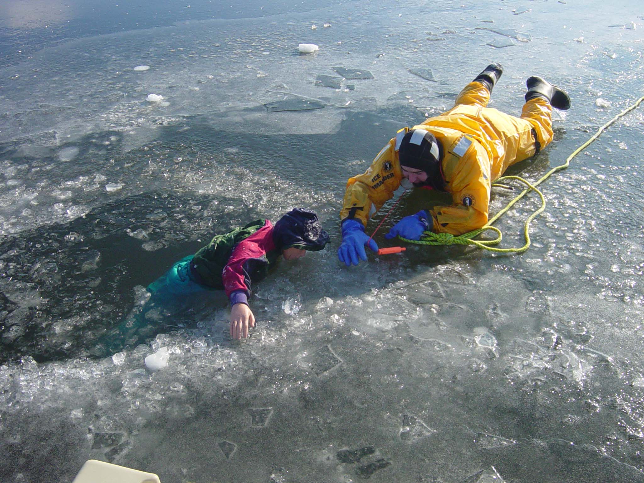 Firefighter practices ice rescue techniques with a child-size mannequin at a winter training drill.