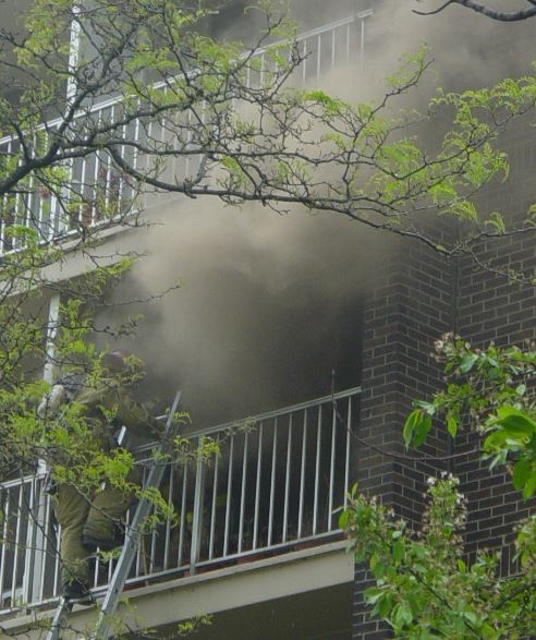 Firefighter climbs a ground ladder to access a balcony at a 4th floor fire.
