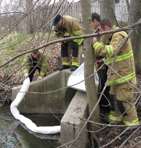  Firefighters and Hazardous Materials technician place boom and pads to absorb an oil spill.